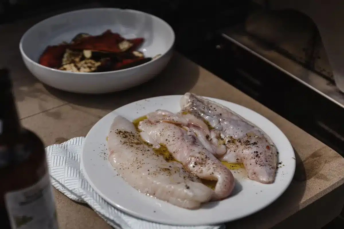 Cooking preparation with olive oil, fresh fish, and colorful vegetables on a kitchen counter