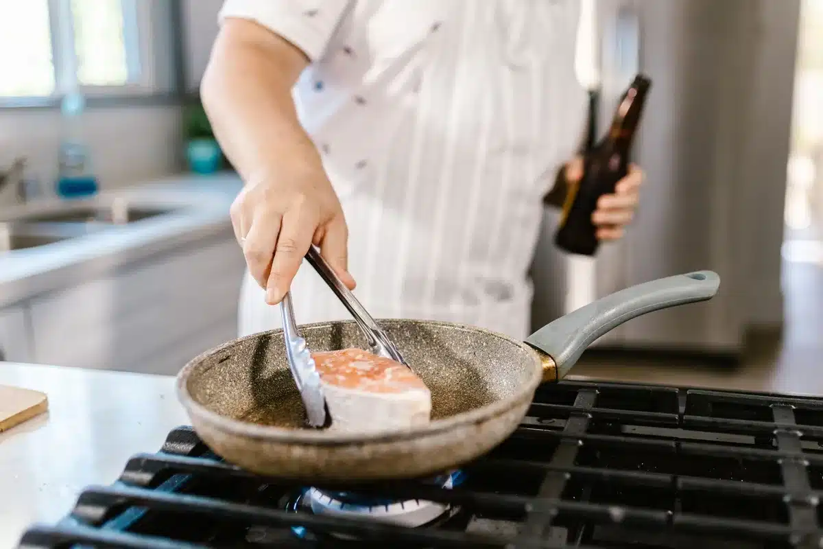 Salmon cakes being pan-seared in a skillet with a golden crust forming