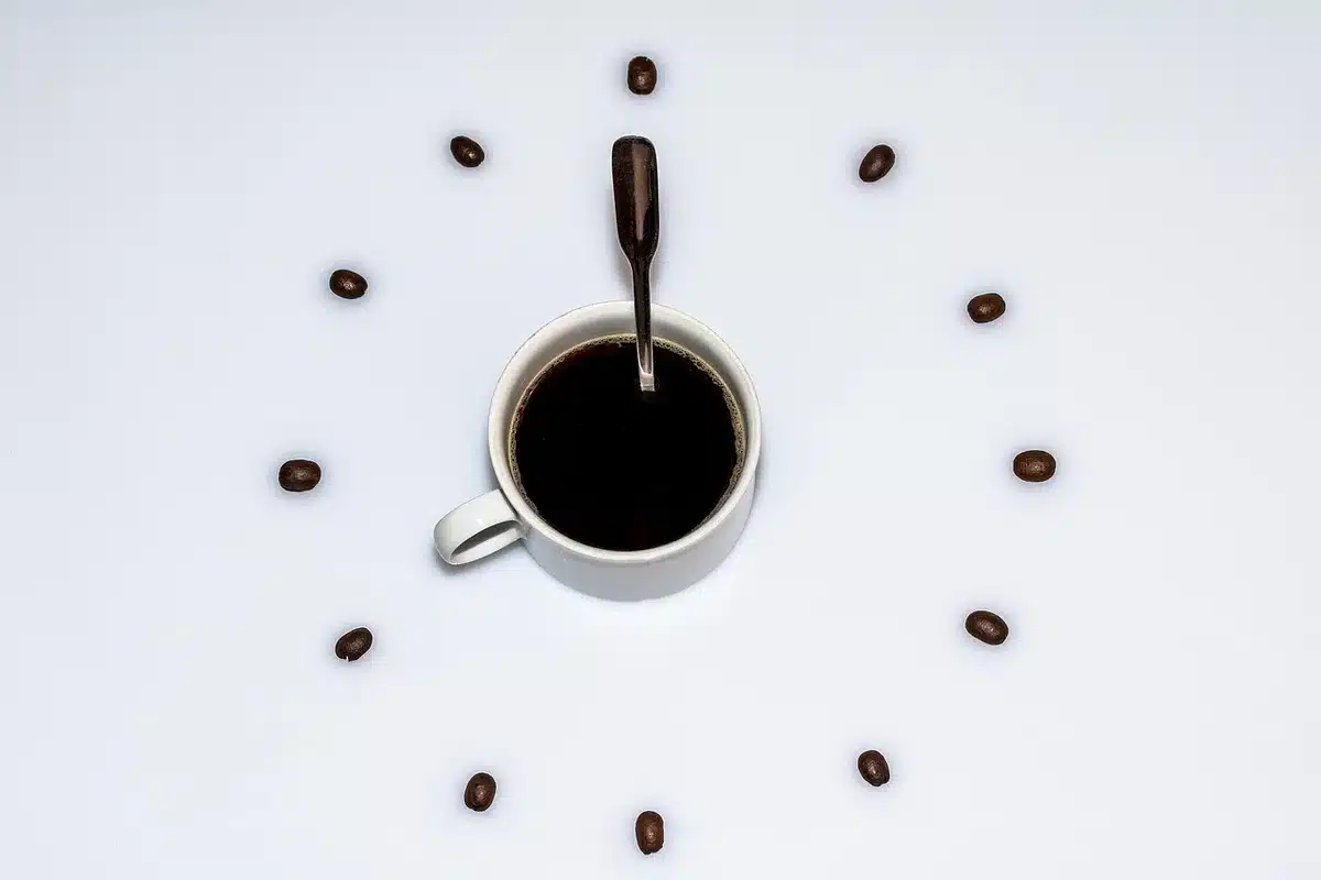 A coffee cup beside a small clock showing afternoon time, on a bright table