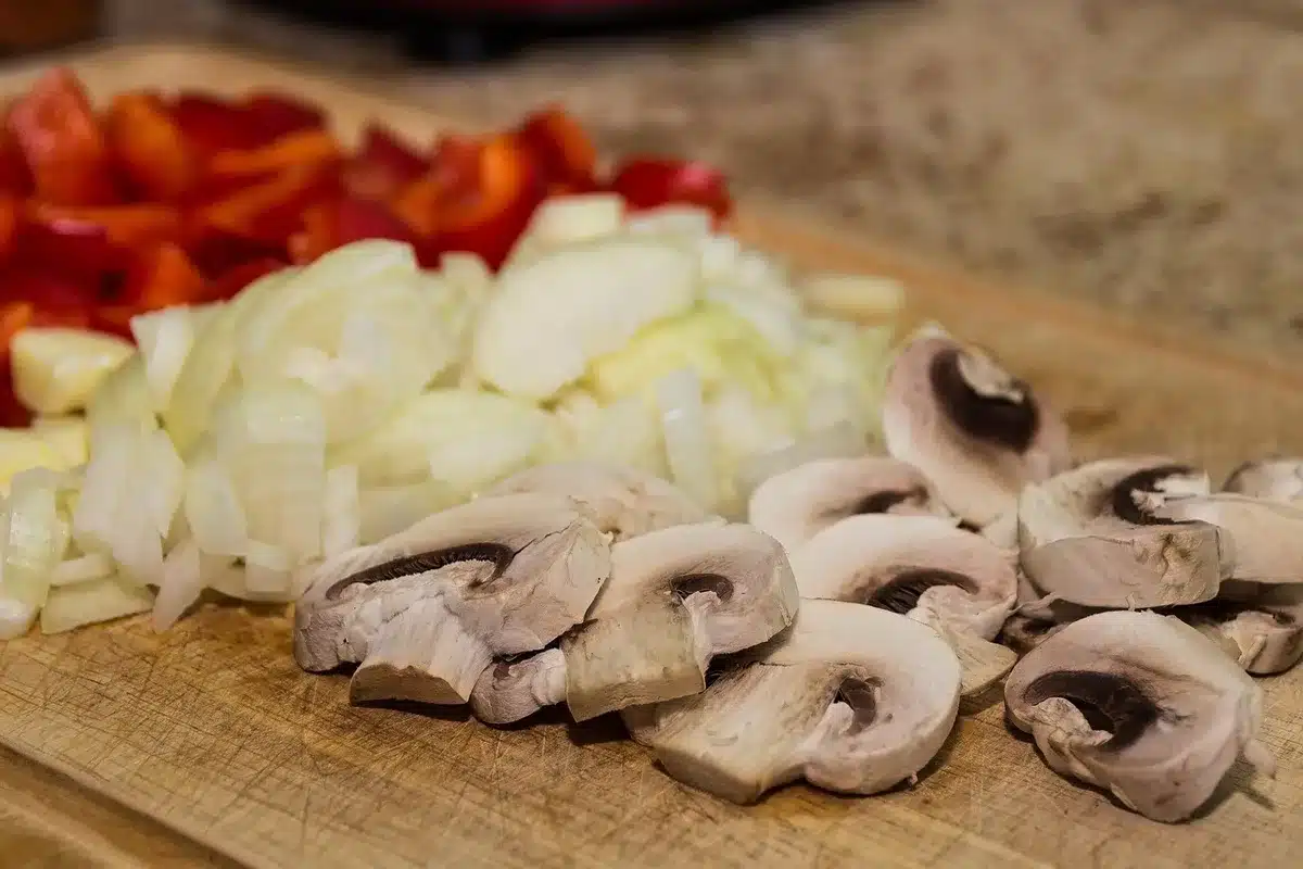 Crushed garlic on a cutting board in a bright kitchen with hands arranging a bowl