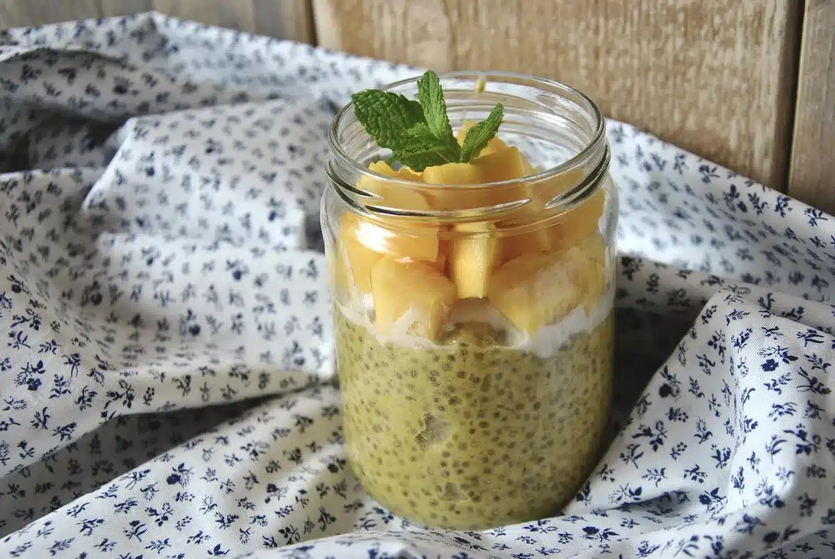 Glass jar of chia pudding beside fruit and a spoon