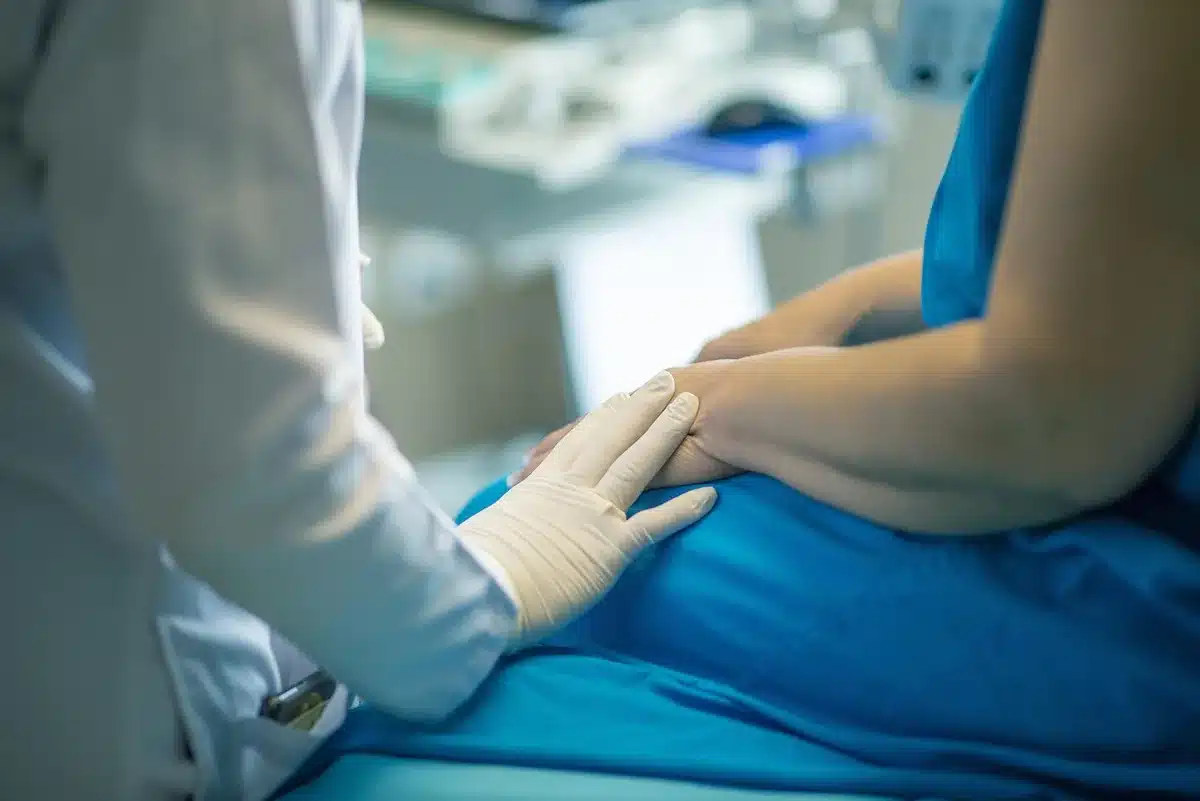Patient hands holding a prescription leaflet and a pillbox on a clinic table in daylight