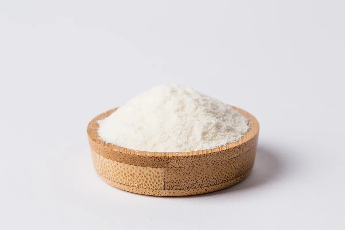 Glass of milk and protein powder scoop on a bright kitchen counter